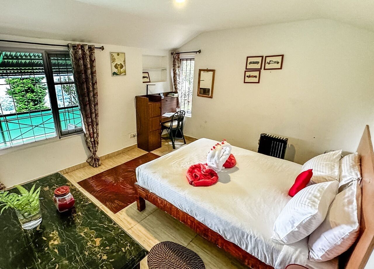 A hotel room with a bed, a desk, a chair, a radiator, and a window with curtains.