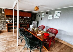 A dining area with a wooden table, black and red chairs, and a stone wall in the background. - Manas Valley View bungalow  (Kodaikanal)