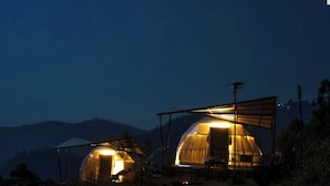 Two dome-shaped tents with a table and chairs in front, set against a mountainous backdrop at night. - Manas Valley View bungalow  (Kodaikanal)