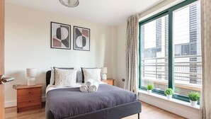 Une chambre moderne avec un grand lit, des tables de chevet, une fenêtre avec des rideaux et deux œuvres d’art abstraites encadrées accrochées au mur.