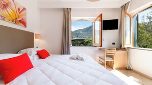 Habitación de hotel con cama, escritorio, televisión y ventana con vista a las montañas.