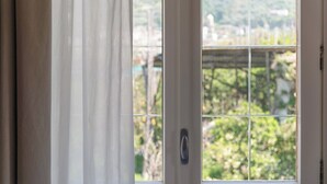 Una puerta blanca con un ventanal de vidrio, un picaporte metálico y vistas a áreas verdes y edificios.