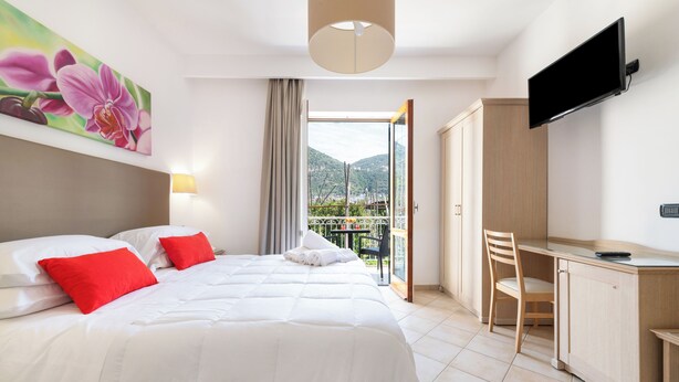 Habitación de hotel con cama, escritorio, televisión y balcón con vistas a las montañas.