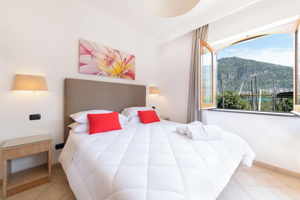 A hotel room with a large bed, two bedside lamps, a painting, and a view of a mountainous landscape.