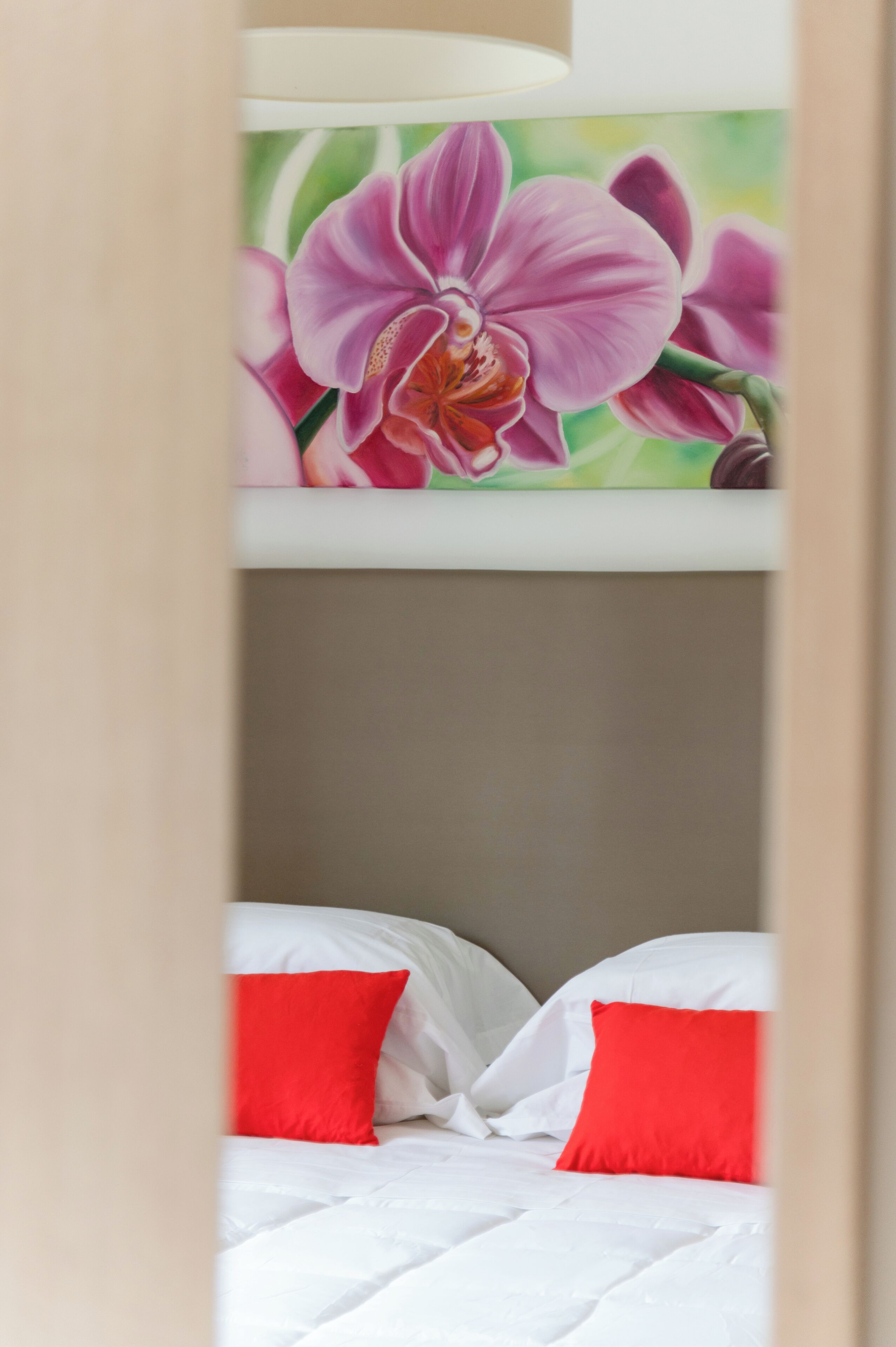 A bunk bed with white bedding and red pillows, and a floral mural above it.