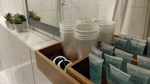 A bathroom with a wooden drawer containing clear plastic containers and a shower area with a glass door. - Cozy studio guest house near the center & trade fair (Nürnberg)