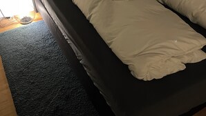 A single bed with a dark frame, white bedding, and a small window with blinds. - Cozy studio guest house near the center & trade fair (Nürnberg)