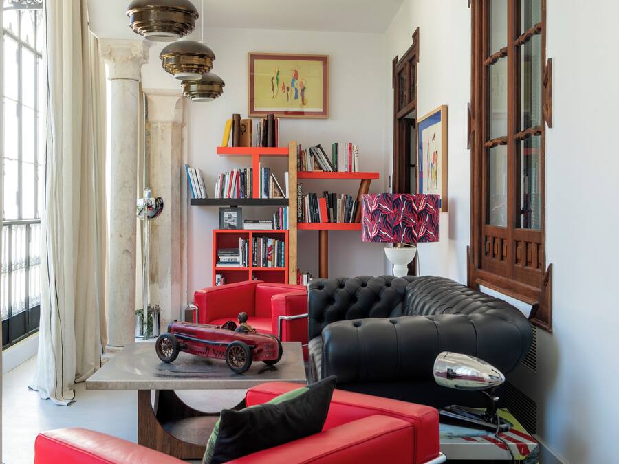 A living room with a red sofa, a black leather couch, and a red armchair. There is a bookshelf with books and a small red car model on a table.