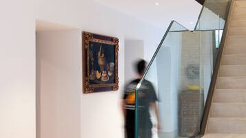 A modern interior with a glass railing staircase, a framed artwork on the wall, and a person walking.