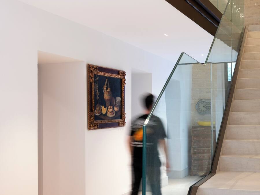 A modern interior with a glass railing staircase, a framed artwork on the wall, and a person walking.
