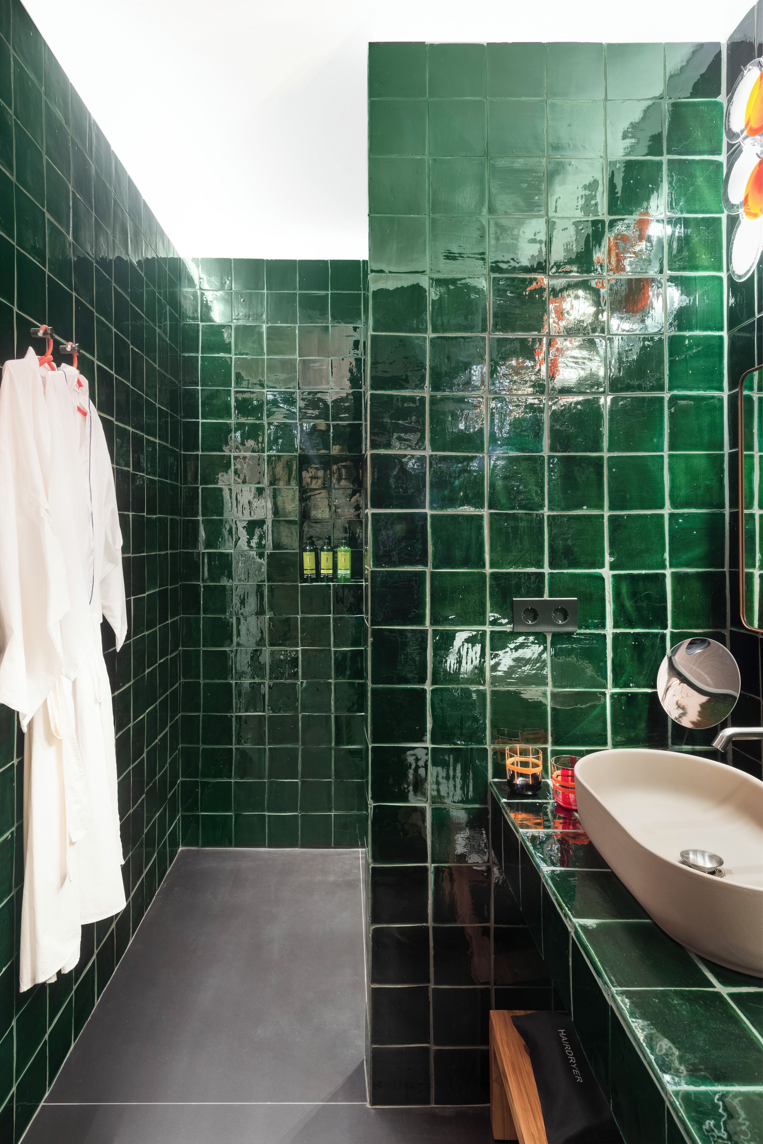 Un baño con azulejos verdes, un lavamanos blanco y un perchero para toallas.