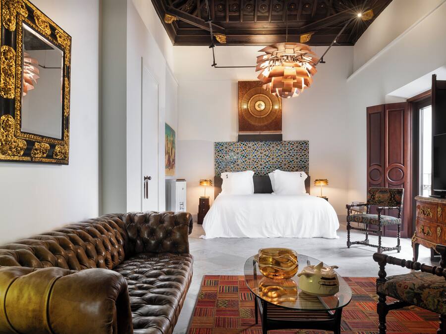 A hotel room with a large bed, a leather sofa, a television, and a decorative mirror.