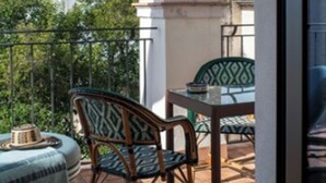 Ένα μπαλκόνι με ένα τραπέζι και καρέκλες, θέα σε έναν ιστορικό πύργο και ένα καθαρό, γαλάζιο ουρανό.