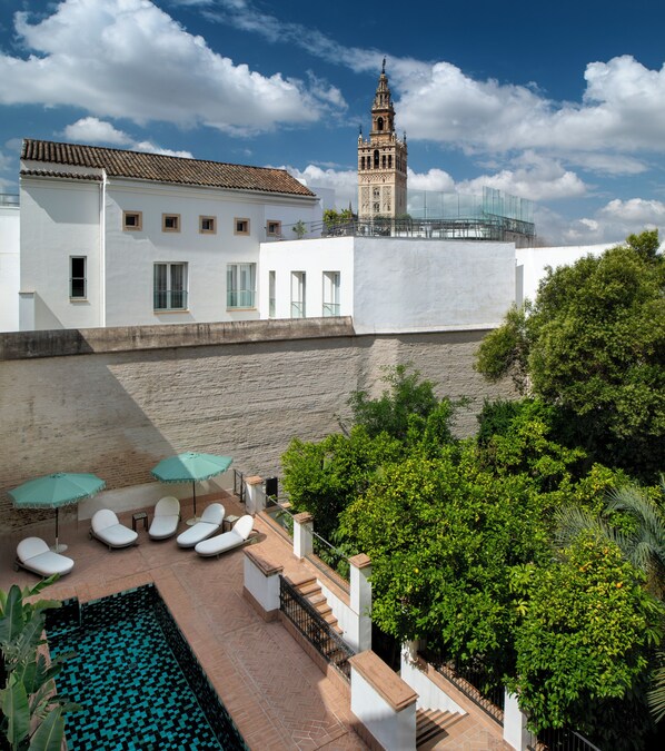 A rooftop pool area with lounge chairs and umbrellas, a staircase leading to a building with a tower, and lush greenery. - Hotel Boutique Casa del Limonero - Adults only (Seville)