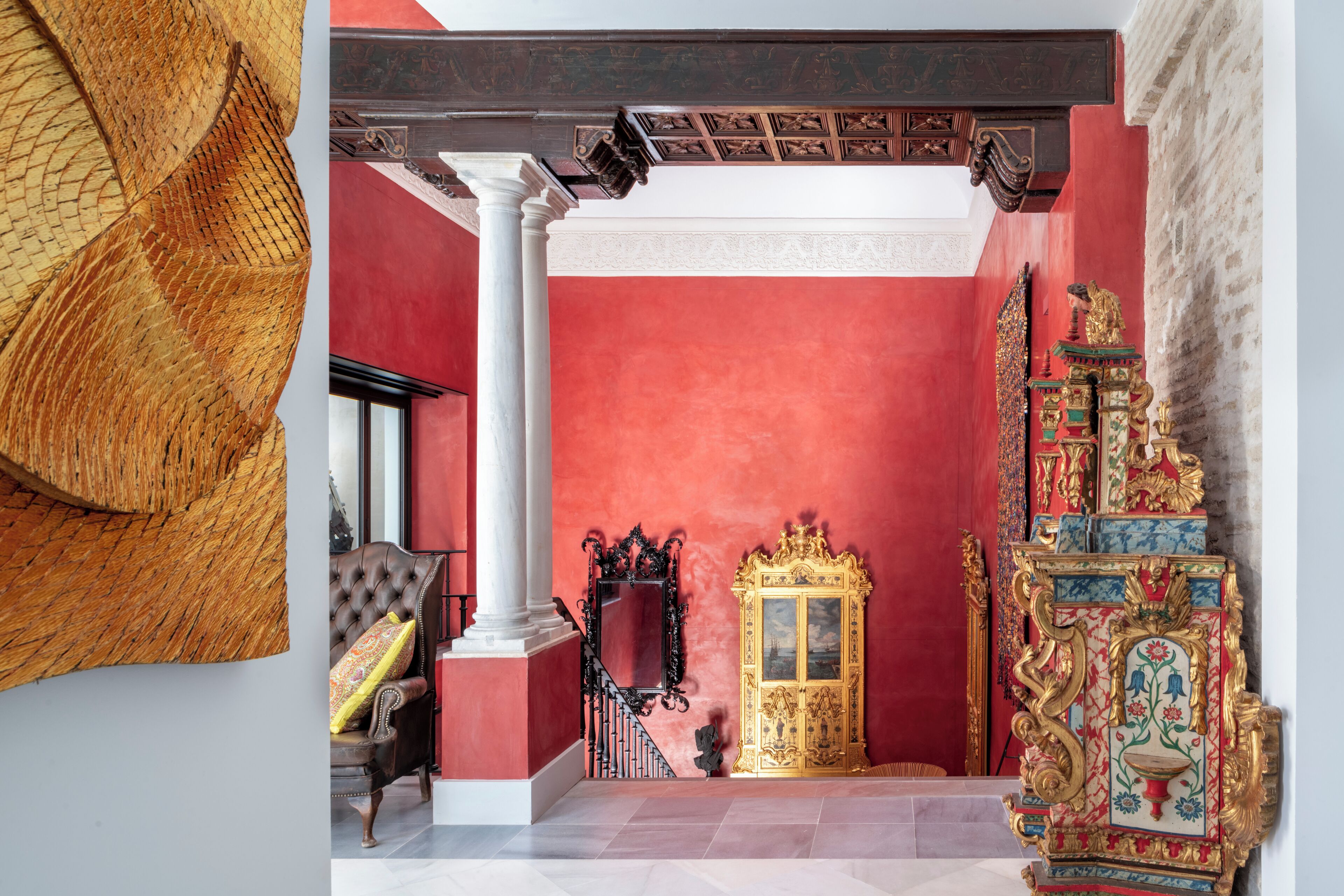 A room with a red wall, a golden ornate cabinet, and a white column.