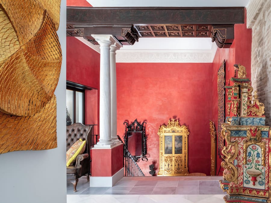 A room with a red wall, a golden ornate cabinet, and a white column.