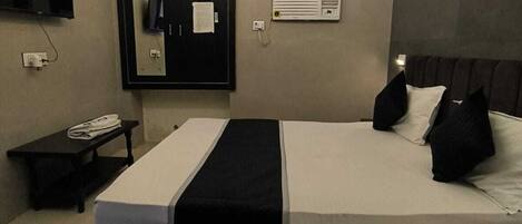 A modern bedroom with a bed, a flat-screen TV, a desk, and a wall-mounted air conditioner.