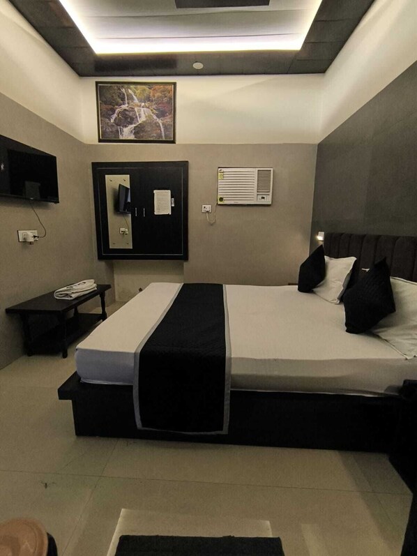 A modern bedroom with a bed, a flat-screen TV, a desk, and a wall-mounted air conditioner. - Hotel Goyal Palace (Agra)