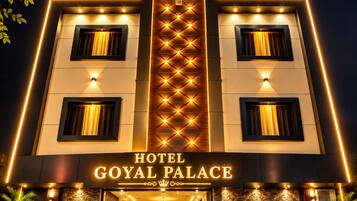 A hotel entrance with a prominent sign reading 'HOTEL GOYAL PALACE' and a modern facade with illuminated windows and a central light fixture.