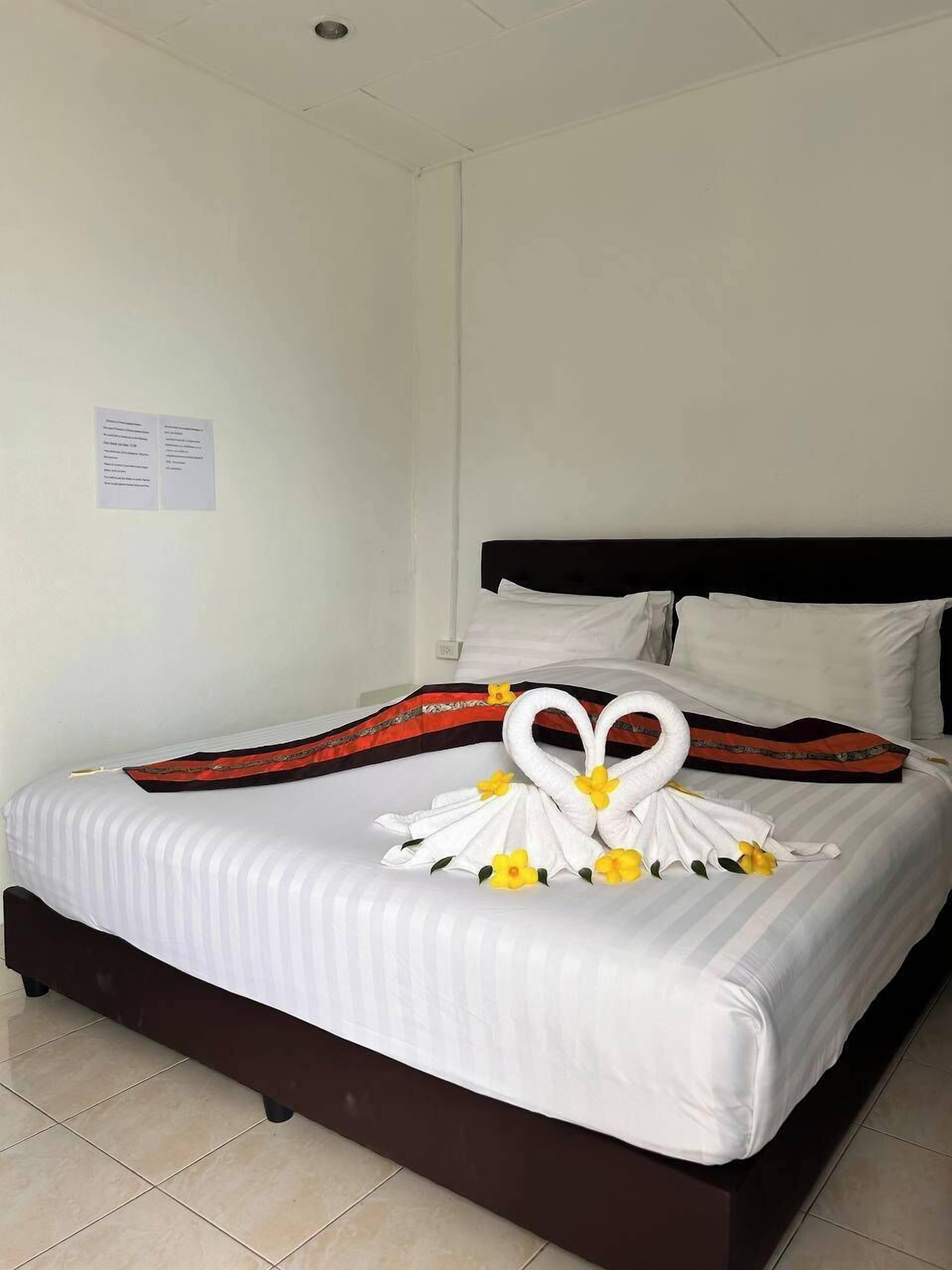 A neatly made bed with a decorative swan towel arrangement and a red and black patterned throw.