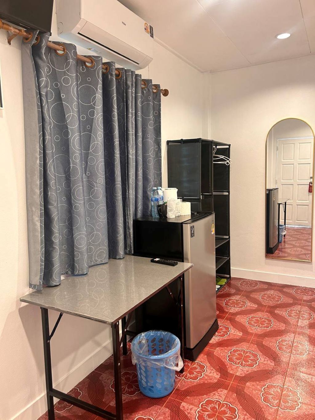 A compact room with a kitchenette, a small table, a trash bin, and a shower area with grey curtains.