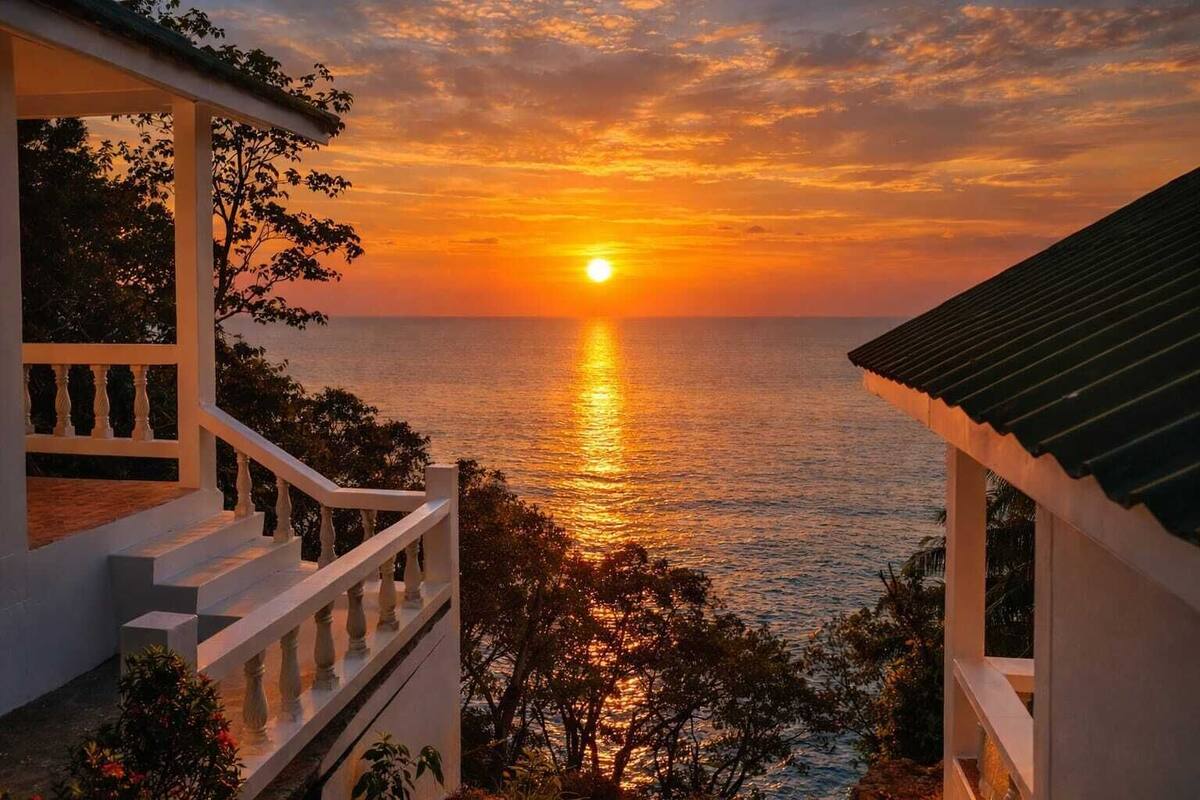 A coastal view with a sunset, a staircase, and a building with a tiled roof.