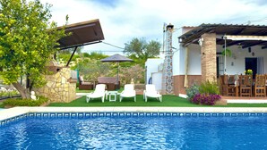 Una piscina con zona de patio, con sillones de descanso y una mesa.