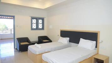 Habitación de hotel con dos camas individuales, un escritorio pequeño, una silla y un ventanal.