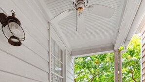 Eine Veranda mit zwei Korbstühlen, einem Deckenventilator und Blick auf Bäume.