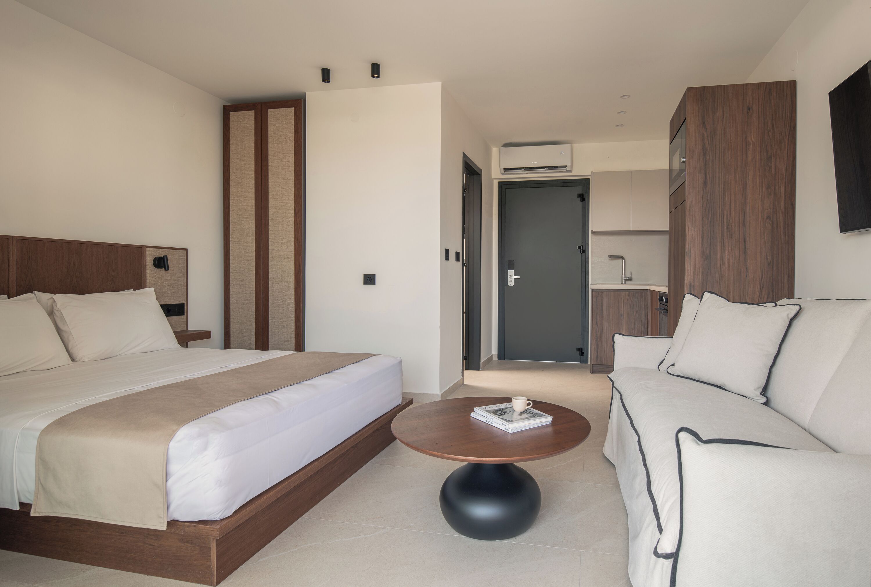 A modern hotel room with a large bed, a sofa, a round coffee table, and a wardrobe.