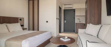 A modern hotel room with a large bed, a sofa, a round coffee table, and a wardrobe.