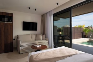 Habitació d'hotel moderna amb un llit, un sofà, una taula de cafè, un televisor i una porta corredissa de vidre que dona a una zona de piscina.