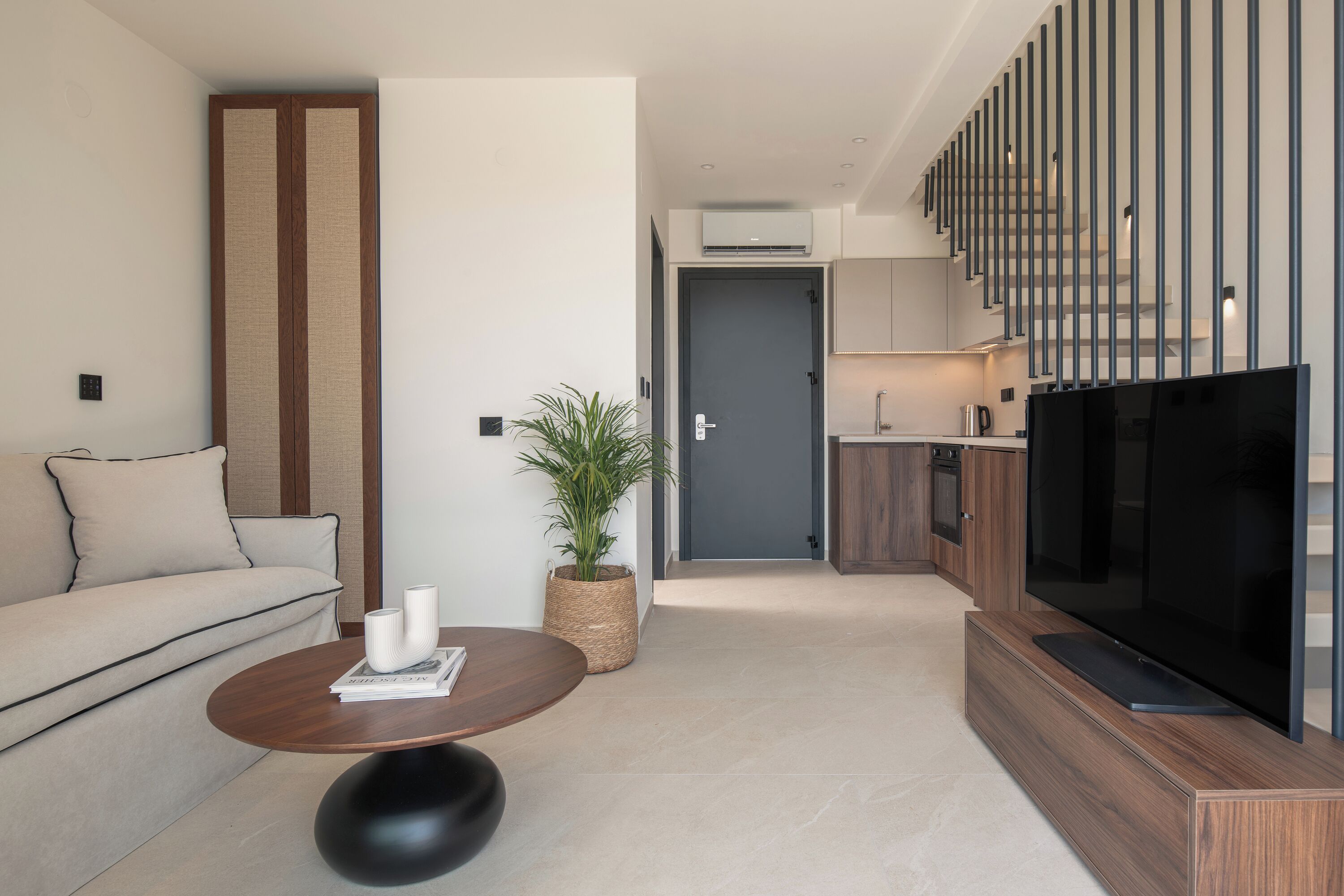 Uma sala de estar moderna com um sofá, uma mesa de centro, uma TV e uma área de cozinha ao fundo.
