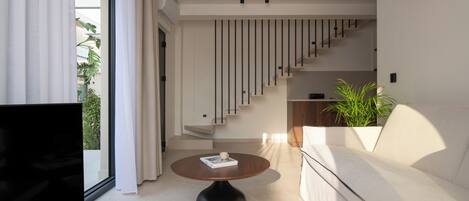 A modern living room with a flat-screen TV, a round coffee table, a sofa, and a staircase leading to an upper level.
