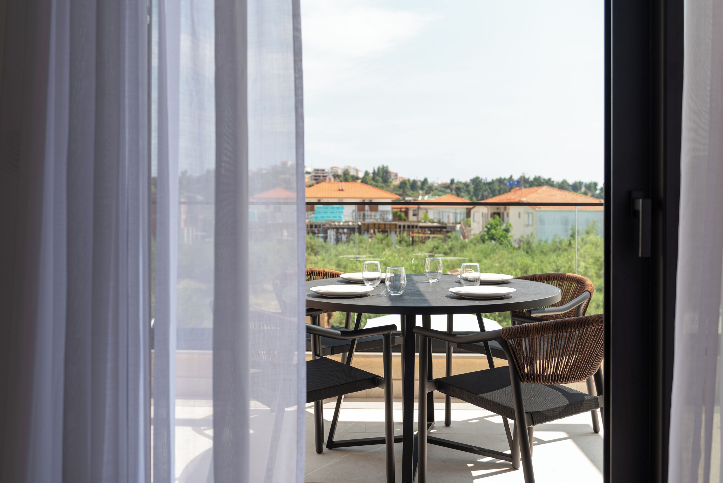 Een terras met een tafel voor vier personen, omringd door rieten stoelen, met uitzicht op een woonwijk met huizen en groen.