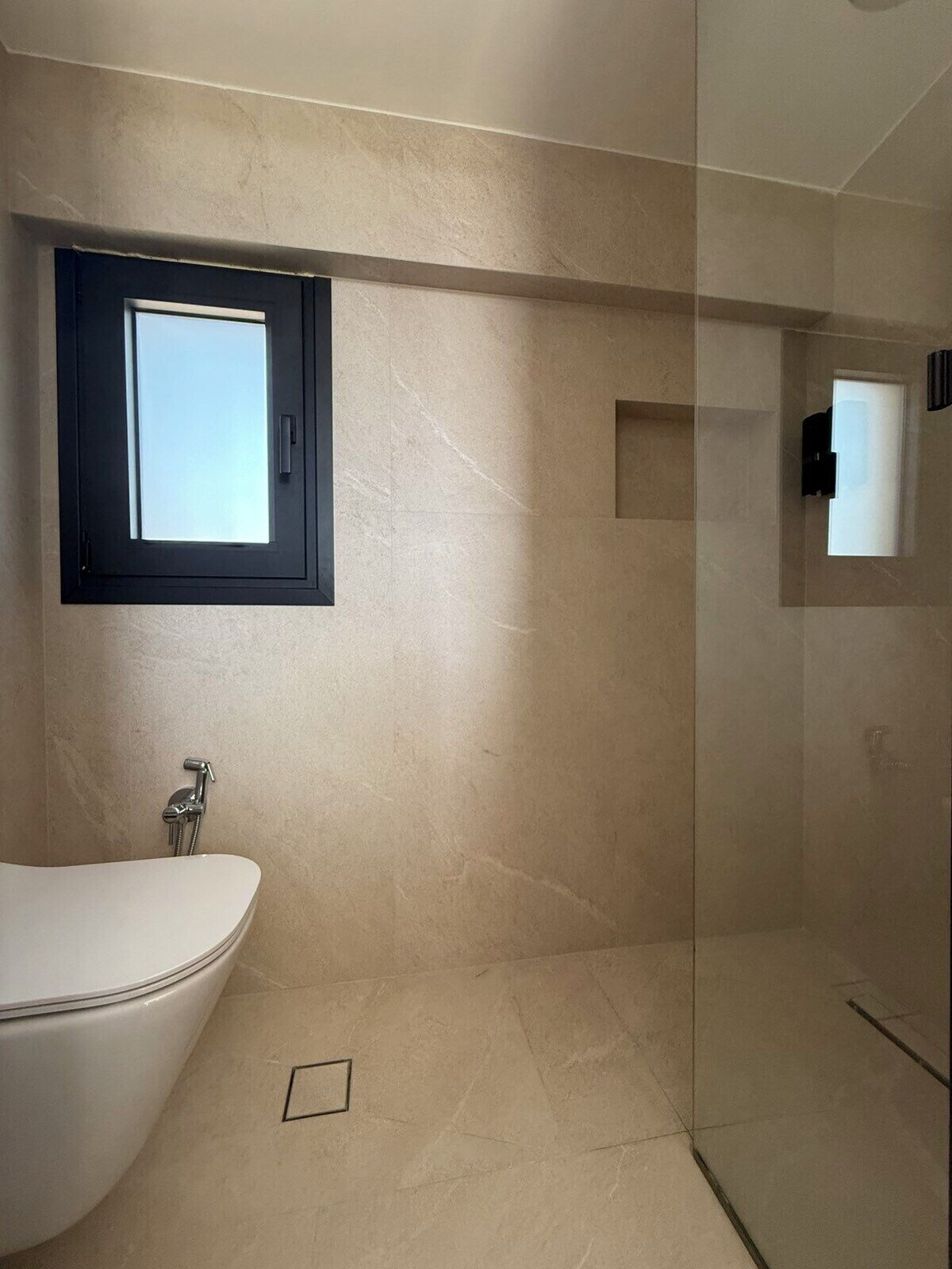 A modern bathroom with a freestanding bathtub, a glass-enclosed shower, and a small window providing natural light.