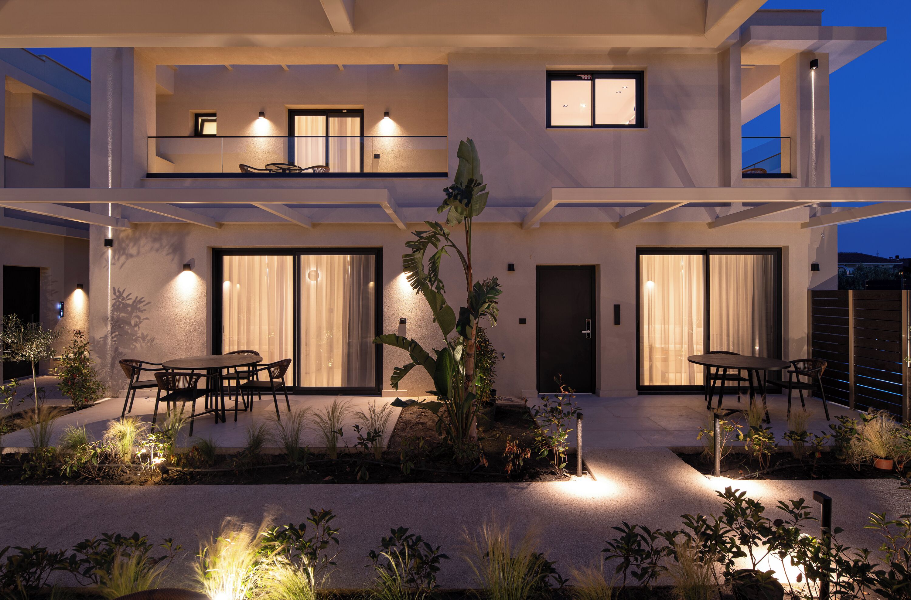 A modern two-story house with a patio area featuring outdoor furniture and plants.