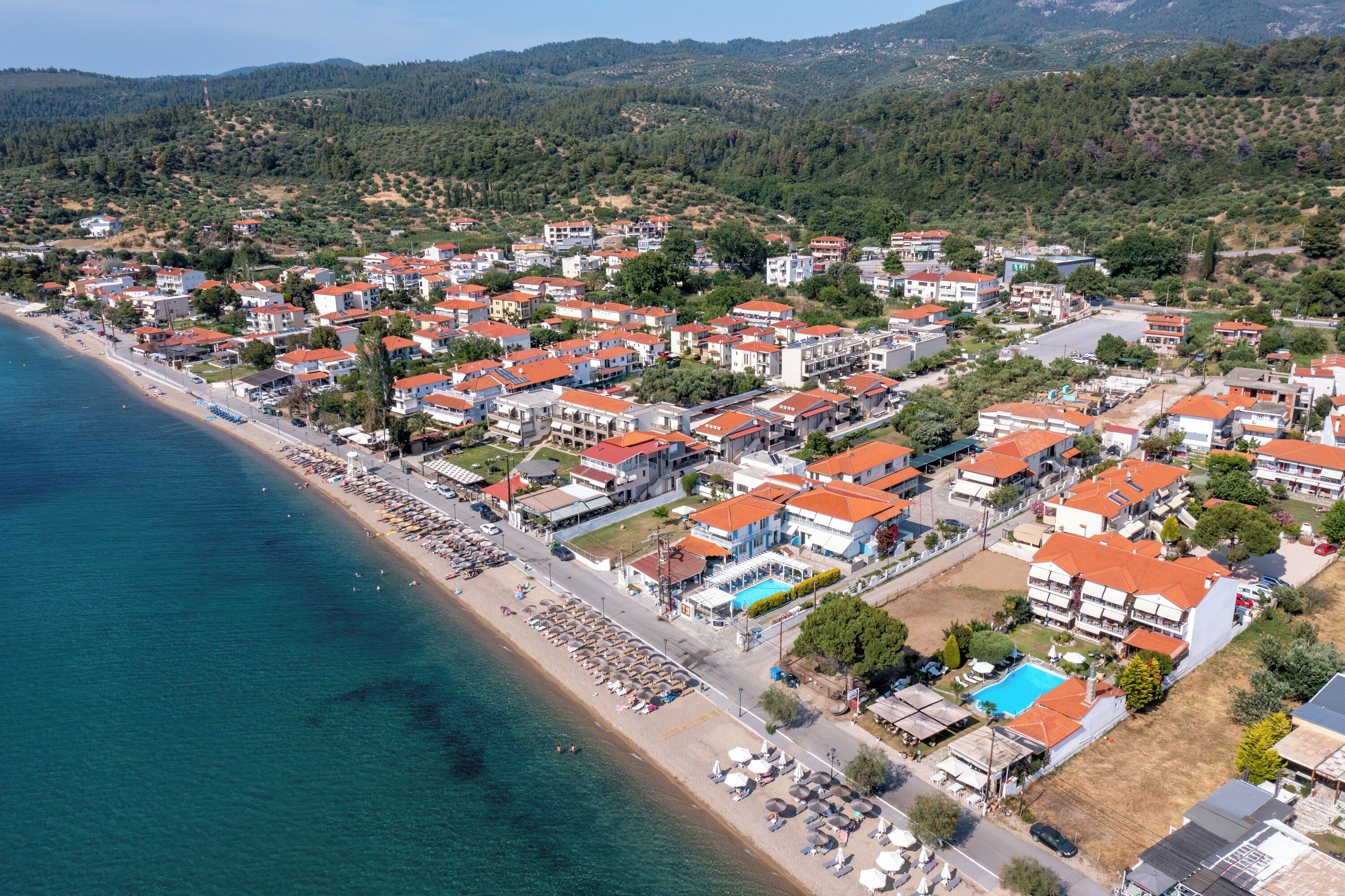 Vista aérea de un pueblo costero con playa, edificios residenciales y una piscina.