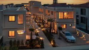 A modern residential building with a rooftop terrace, a car parked in front, and a sign that reads "VISTA".