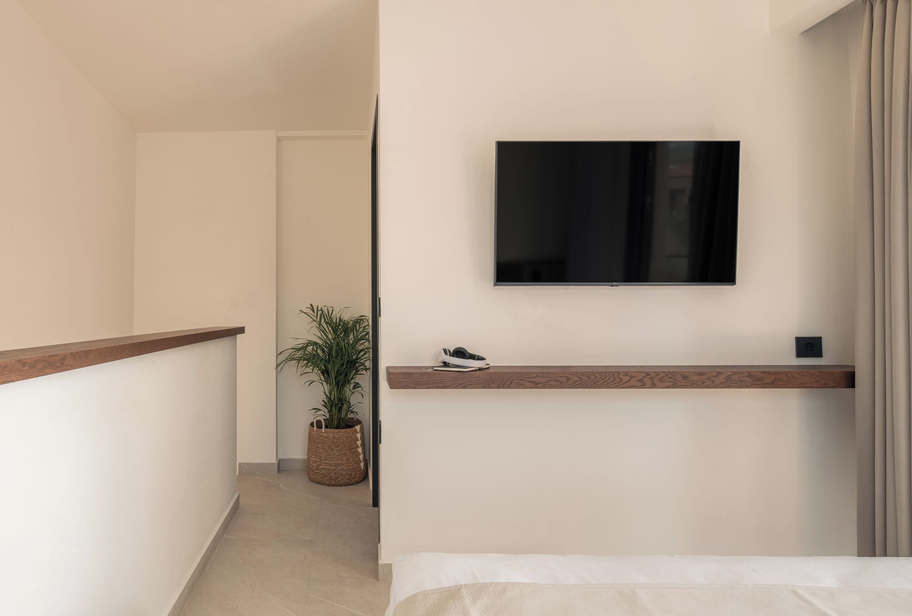 A hotel room with a bed, a mounted TV, a shoe rack, and a potted plant.