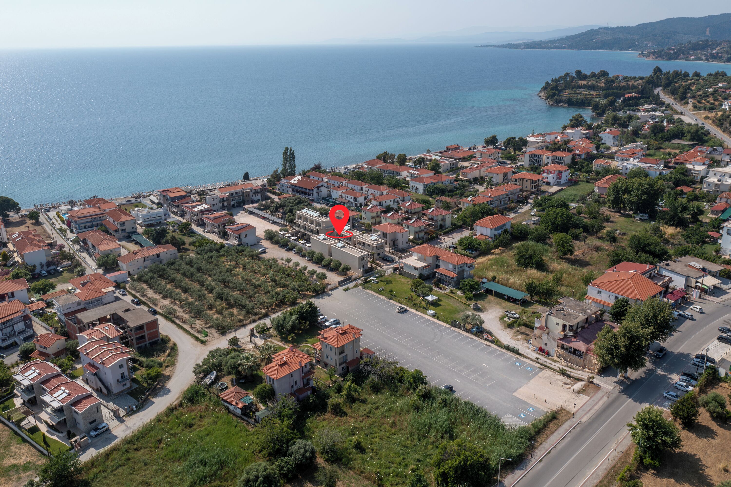 Vue aérienne d’un quartier résidentiel situé sur la côte, avec des maisons, un parking et une route menant à la mer.