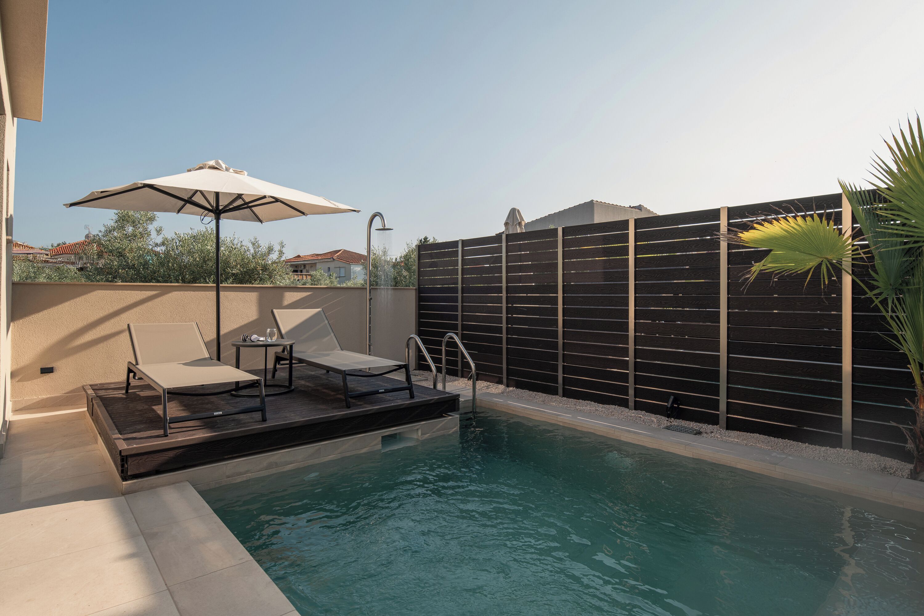 En swimmingpool med solterrasse, liggestole og parasol.