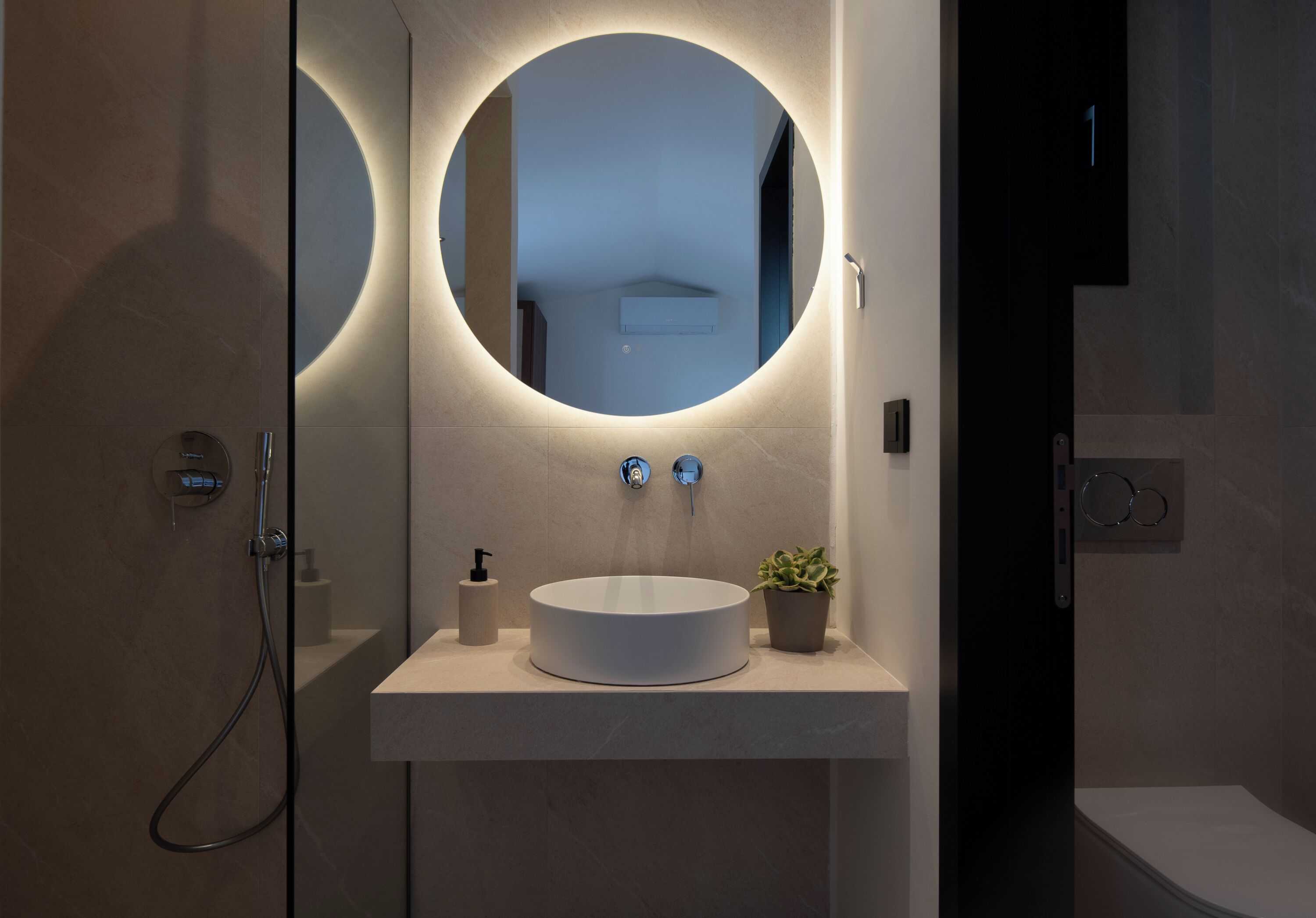 A modern bathroom with a round mirror, a white sink, and a small potted plant.