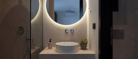 A modern bathroom with a round mirror, a white sink, and a small potted plant.