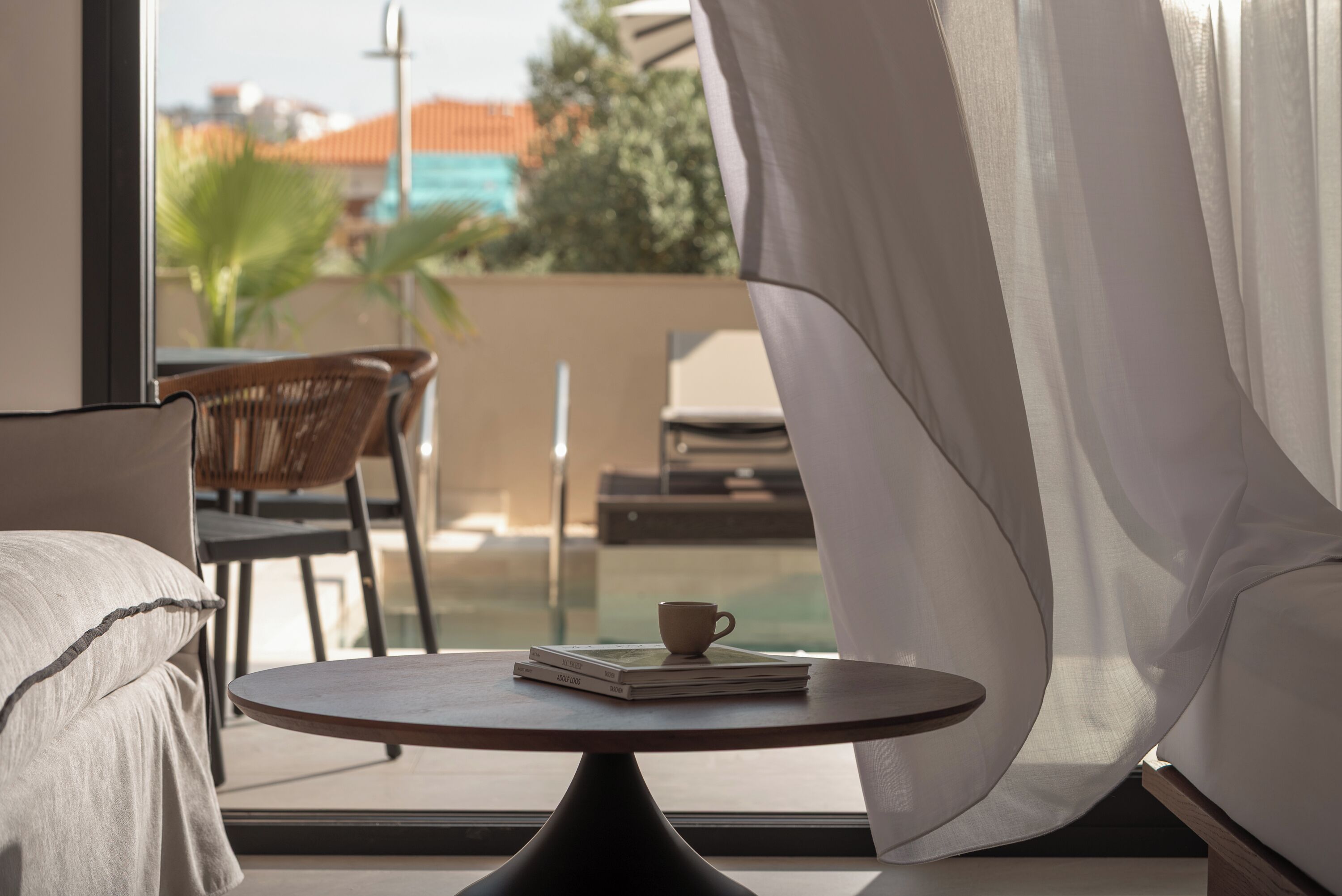 Una habitación con una mesa redonda, una silla, un sofá y un ventanal con cortinas.