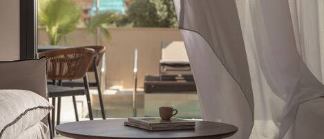Una habitación con una mesa redonda, una silla, un sofá y un ventanal con cortinas.