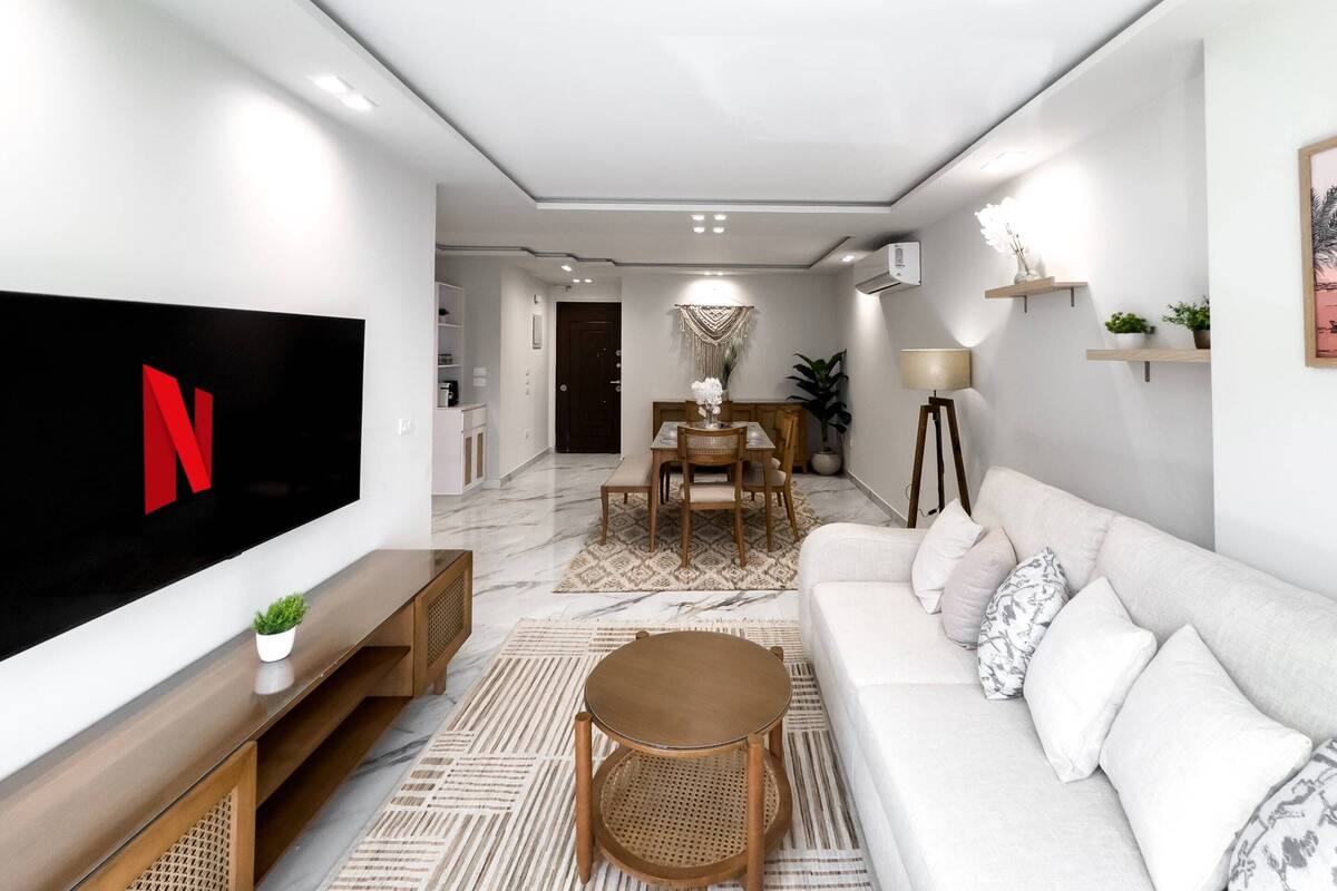 Ein modernes Wohnzimmer mit Flachbildfernseher, einer Couch, einem Couchtisch und einem Essbereich mit Tisch und Stühlen.