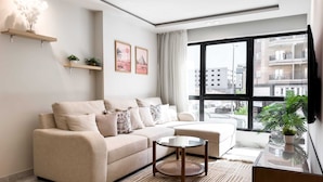 Una sala de estar moderna con un sofá beige, una mesa de centro de vidrio y un ventanal con vistas a la ciudad.