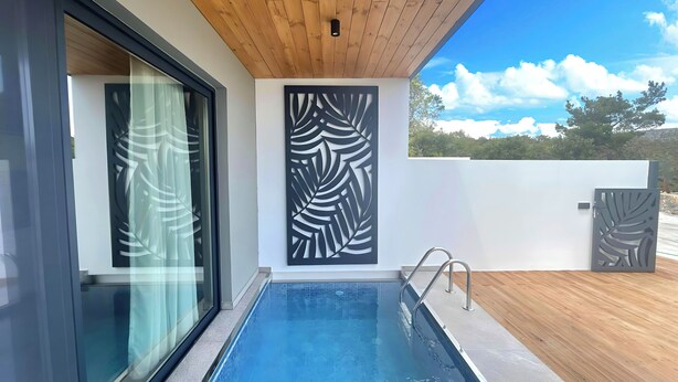 Un área de piscina exterior moderna con muelle de madera, cerramiento de vidrio y un panel decorativo.