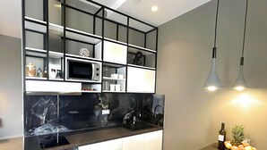Una cocina moderna con microondas integrado, un lavamanos y una encimera. Se observa un refrigerador, una mesa de comedor con frutero y lámparas colgantes.